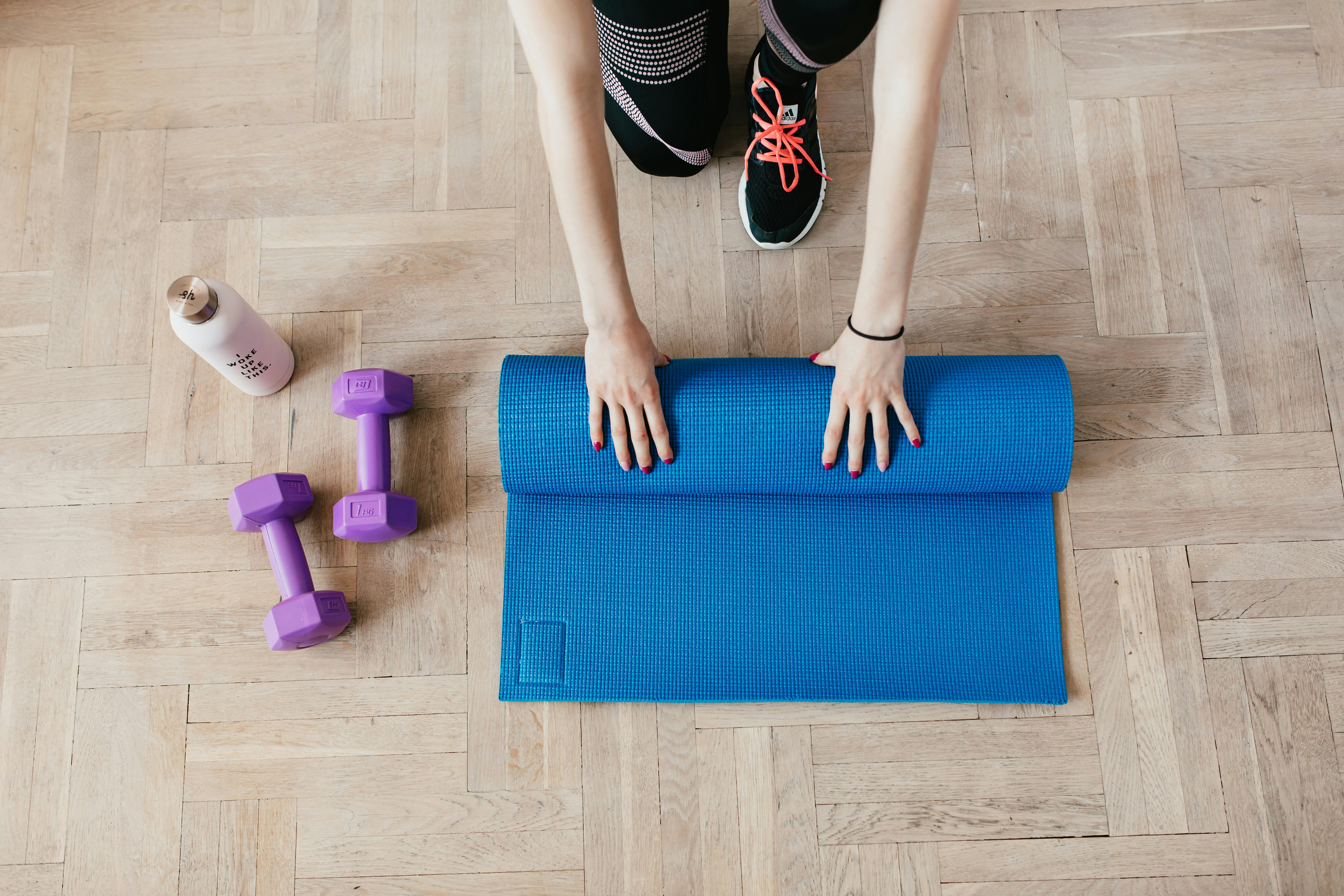 Top view of anonymous female athlete in black leggings and sneakers unfolding blue mat for exercisin