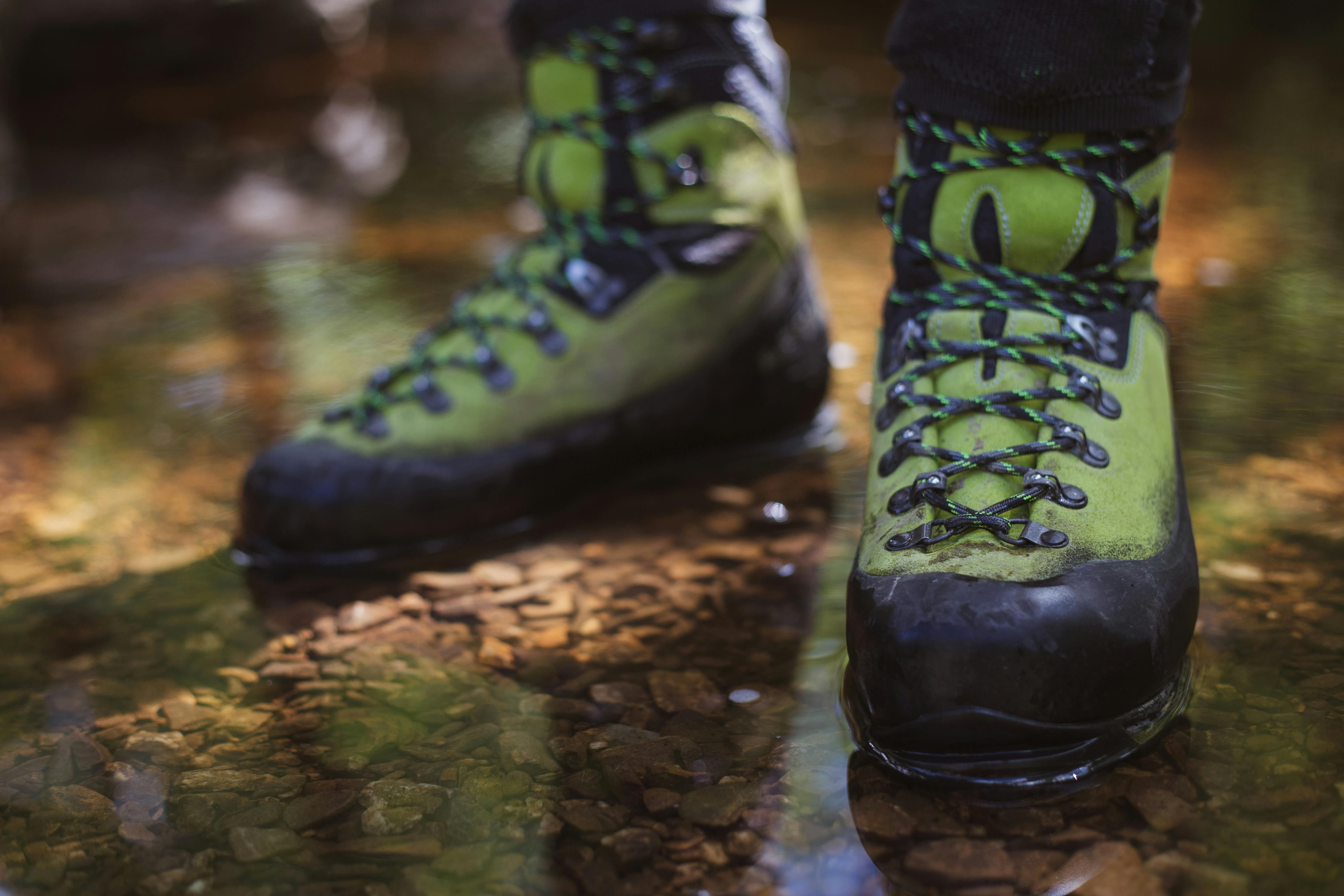 Green hiking boots in a shallow stream, perfect for outdoor adventures.