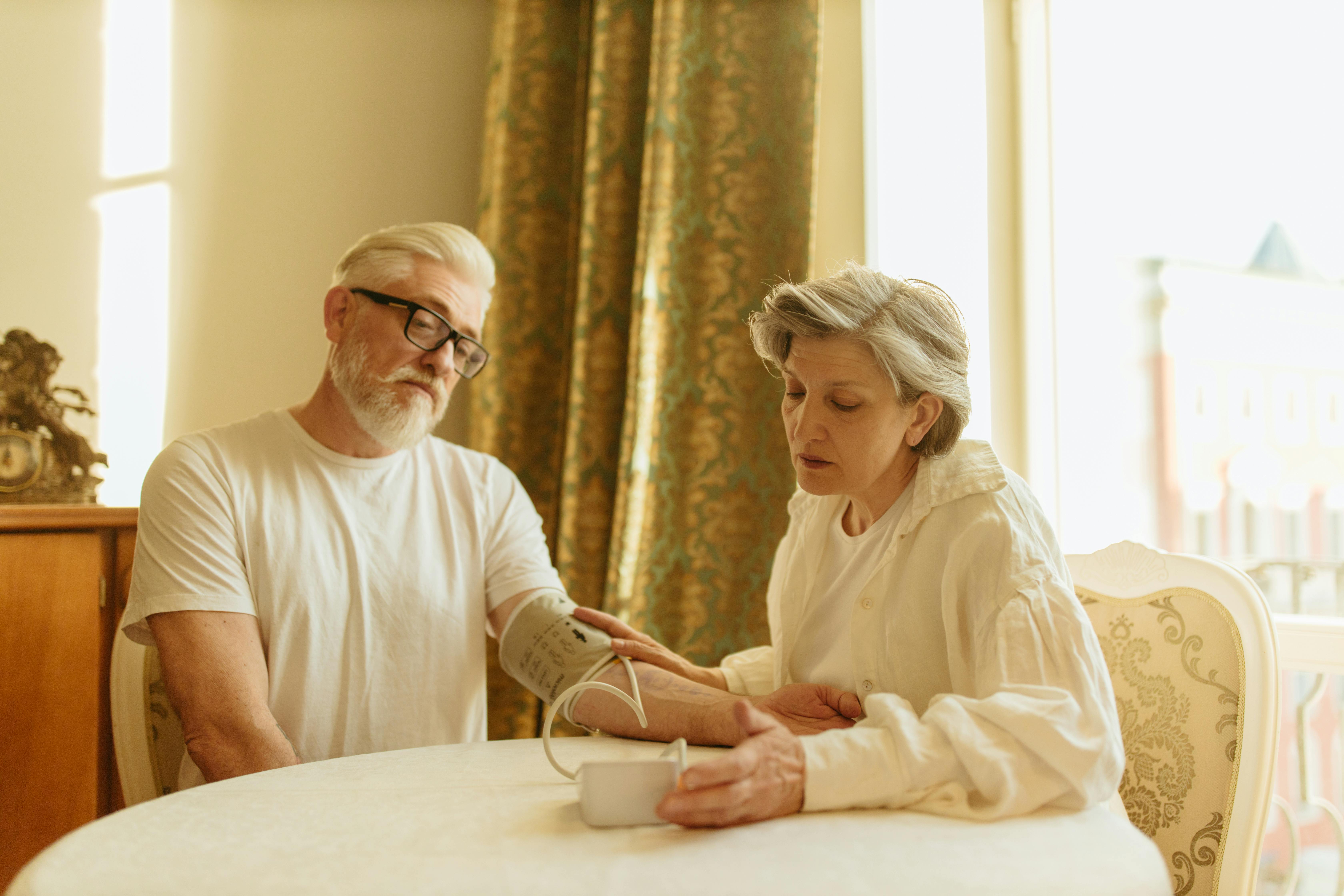 An elderly couple at home measuring blood pressure with a digital monitor, depicting care and health